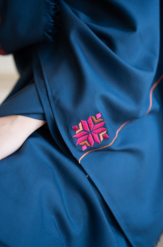 A woman draped in a blue shawl adorned with intricate pink embroidery, showcasing elegance and cultural artistry.
