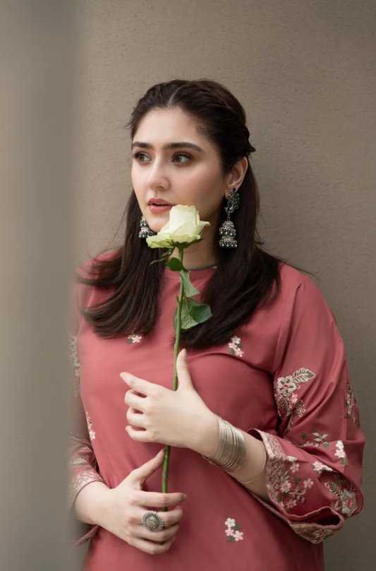 A woman in a pink dress gracefully holds a single rose, showcasing elegance and beauty in a serene setting.