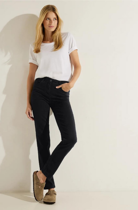 A woman dressed in black jeans and a white t-shirt stands confidently, showcasing a casual yet stylish outfit.