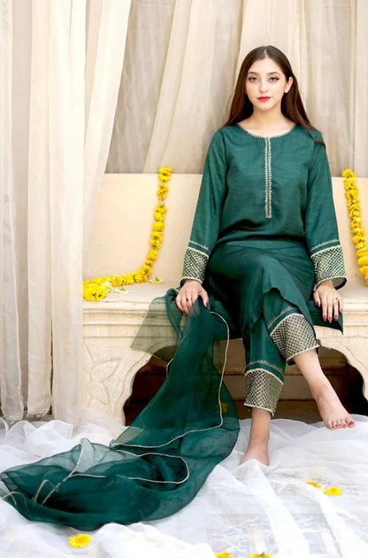 A woman in a green dress is seated gracefully on a bed, exuding elegance and tranquility in her surroundings.