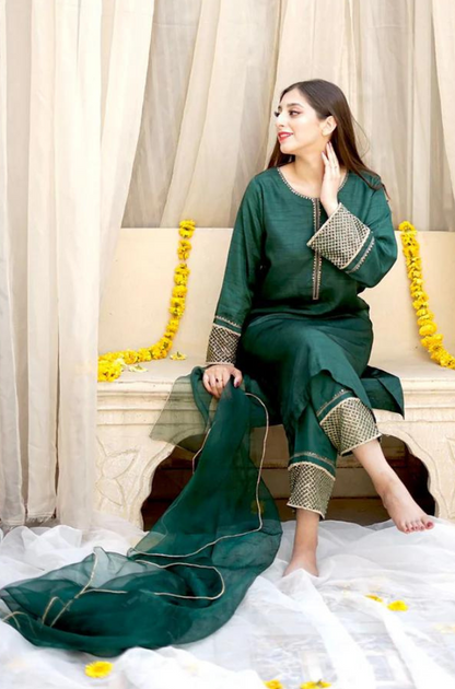 A woman wearing a green dress sits on a bed, embodying a serene and stylish presence in a cozy setting.