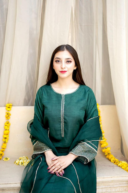 A woman in a green dress is perched on a bed, radiating calmness and sophistication in her environment.