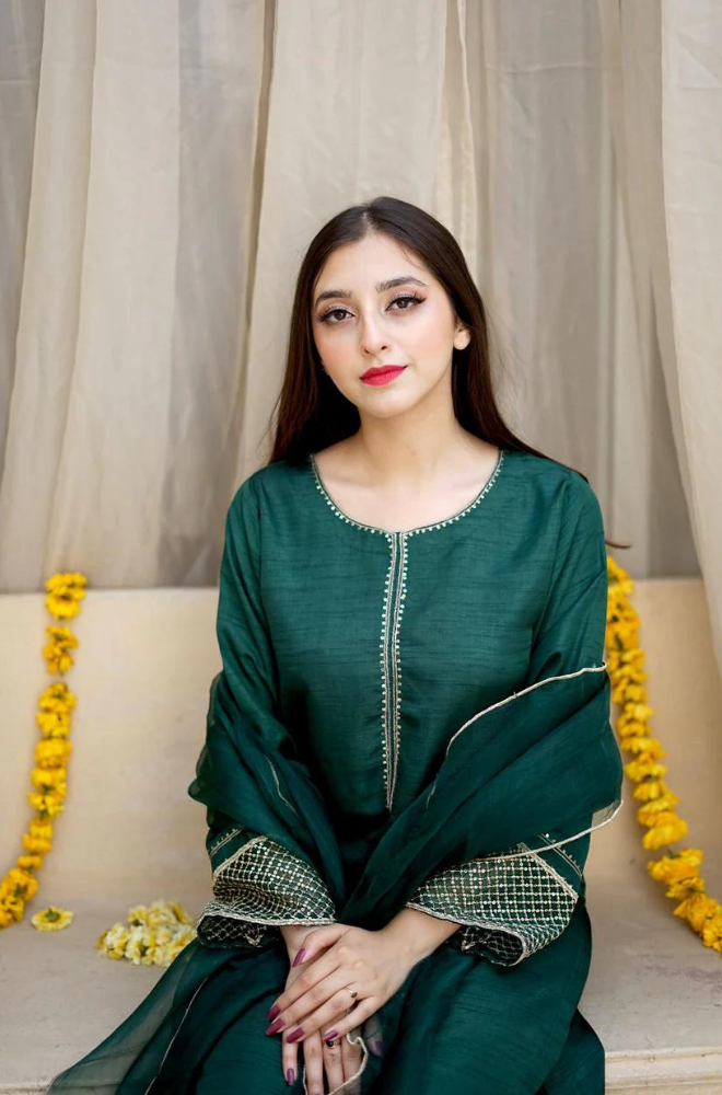 A woman dressed in green sits on a bed, showcasing a blend of elegance and comfort in her peaceful space.
