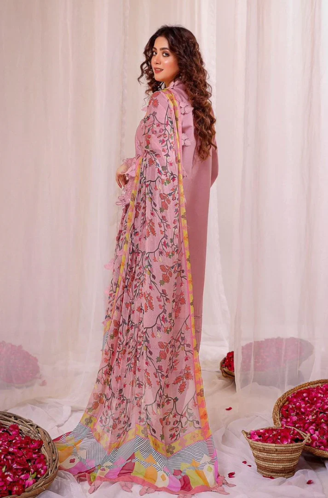 A woman in a pink sari stands beside a beautifully arranged display of flowers.