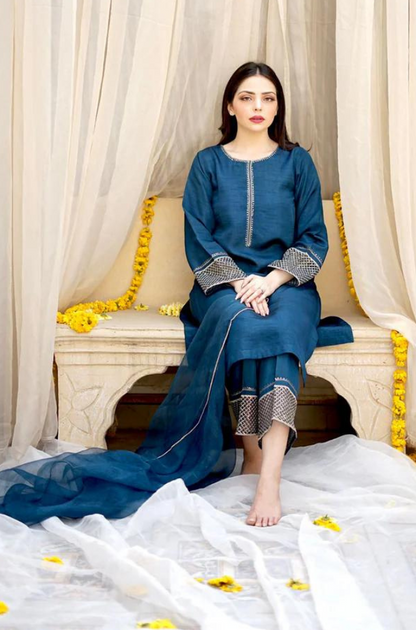  A woman in a blue dress is seated gracefully on a bed, exuding a calm and serene presence in the room.