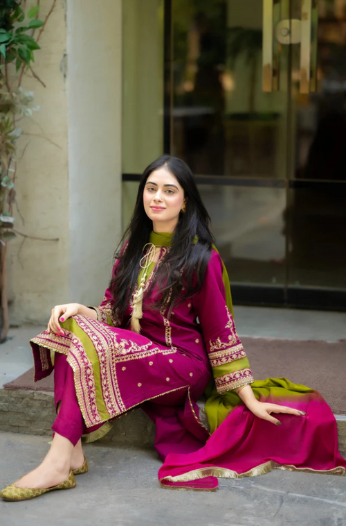  A woman wearing a pink and green outfit sits on outdoor steps, smiling and looking relaxed in a casual setting.