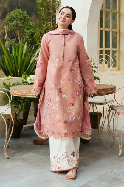 A woman wearing a pink and white embroidered suit, standing confidently with a smile.