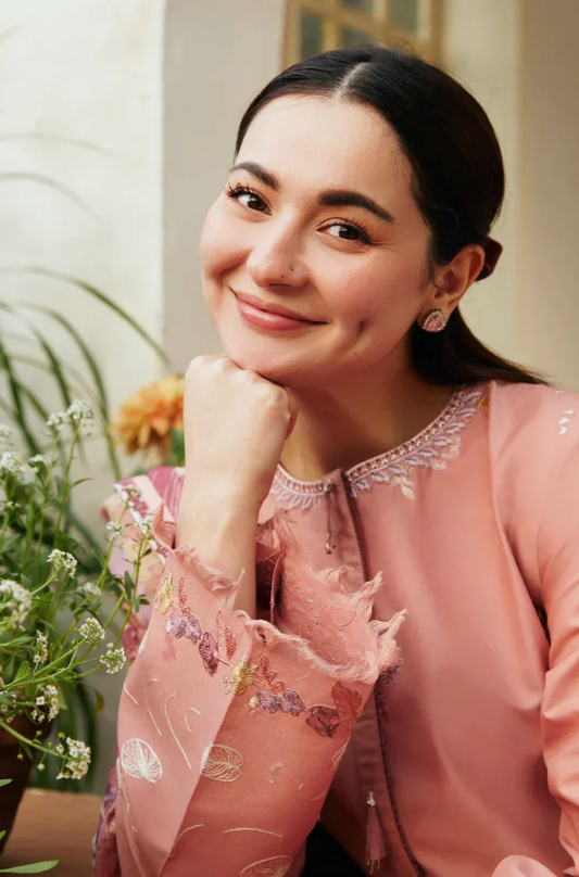 A woman in a pink outfit sits on a chair beside a green plant