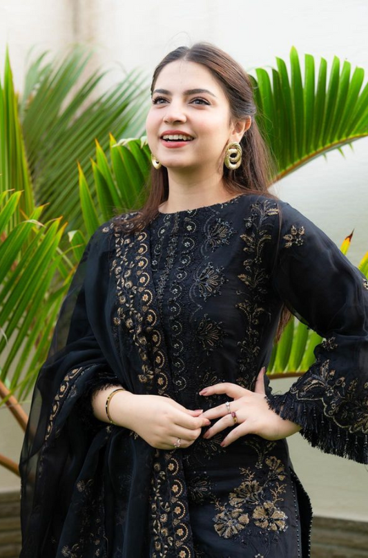 A woman elegantly poses for the camera, wearing a stunning black and gold dress that highlights her graceful silhouette.