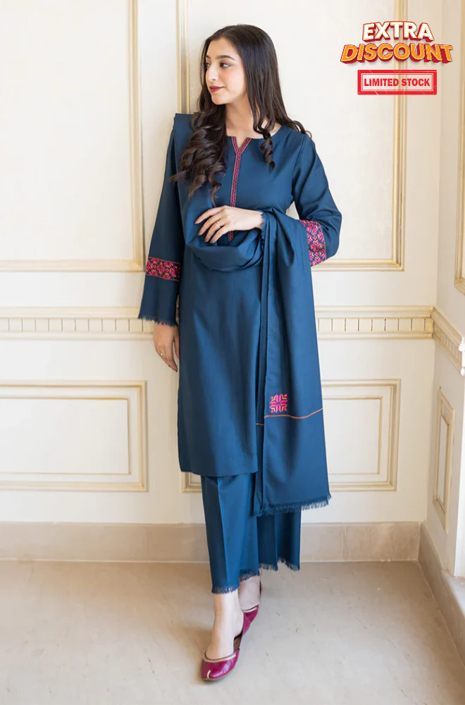 A woman wearing a blue Pakistani suit poses against a wall, highlighting the intricate design of her traditional outfit.