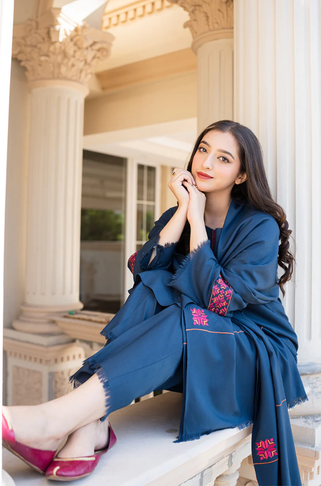 A woman in a blue dress sits gracefully on a ledge, enjoying the view around her.